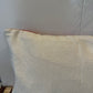 A close-up of a square throw pillow with a textured cream linen cover, showing a hint of red piping along the top edge.