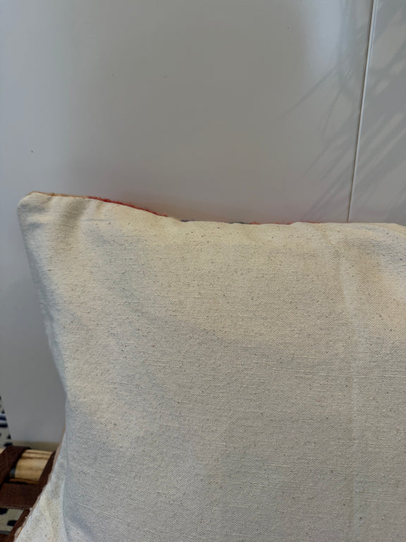 A close-up of a square throw pillow with a textured cream linen cover, showing a hint of red piping along the top edge.
