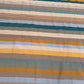A close-up of a striped textile with horizontal bands in beige, brown, muted blue, teal, mustard yellow, and olive green.