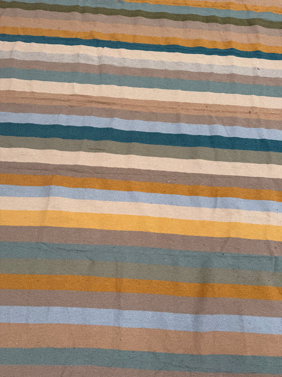 A close-up of a striped textile with horizontal bands in beige, brown, muted blue, teal, mustard yellow, and olive green.