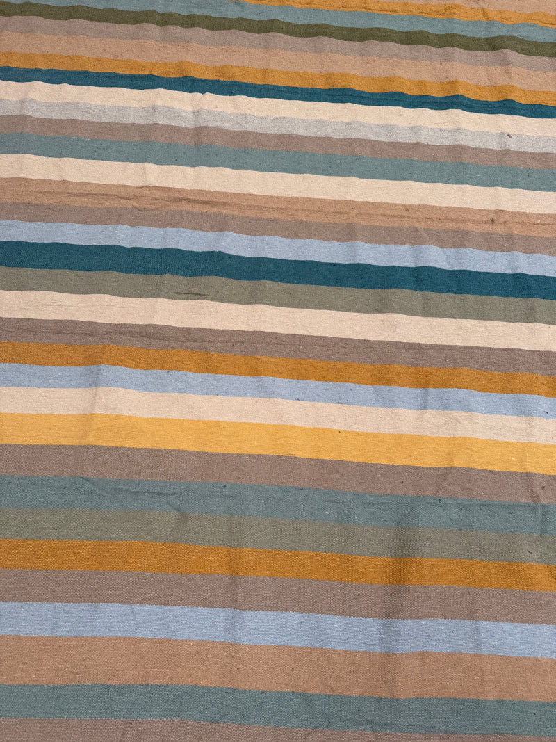 A close-up of a striped textile with horizontal bands in beige, brown, muted blue, teal, mustard yellow, and olive green.